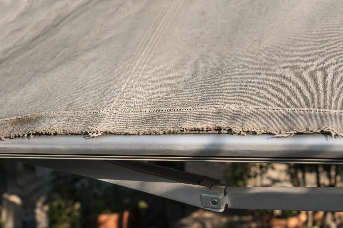 Toile de store banne décolorée et détendue sur une terrasse landaise